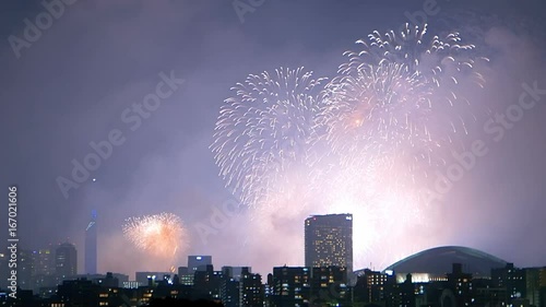 Colorful fireworks exploding in the sky of illuminated urban Fukuoka city.
