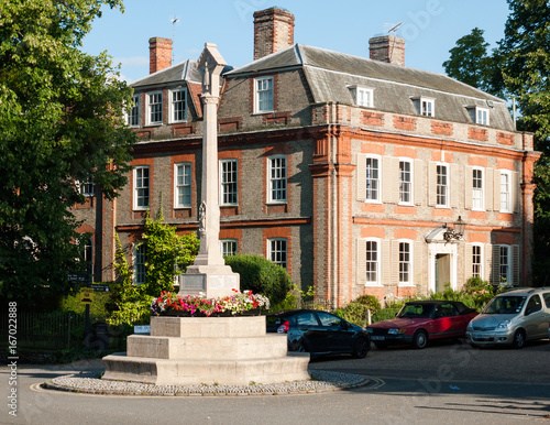 a war memorial landmark in front of a stately home in dedham with some parked cars in summer light close up photo