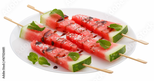 Slices of watermelon with stick on white plate isolated on white background. It looks like ice cream. Decorated with mint leaves, coconut and chocolate syrup. photo