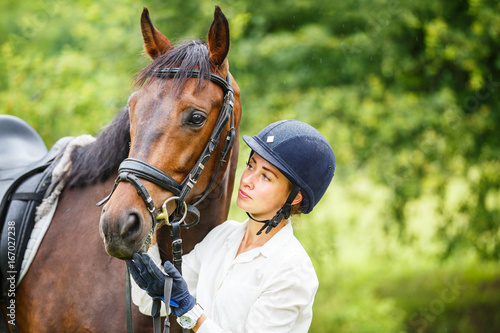 Photographie Jeune femme souriante de cavalier en casque tenant le cheval de la baie par brid