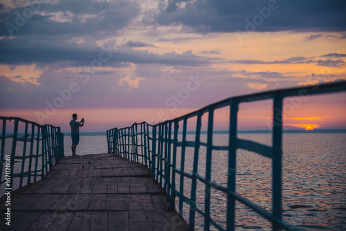 man standing on the pier and looking on sunset