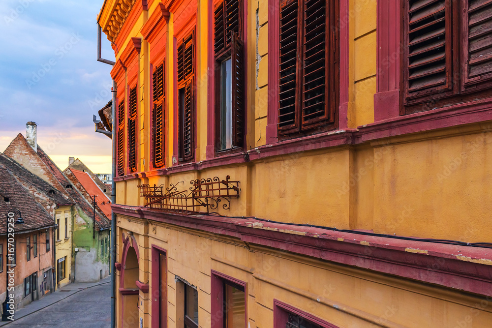 Fototapeta premium Detail of facade with shuttered old windows in ancient house on the street in Sibiu city, Romania, golden sunlight at sunset time