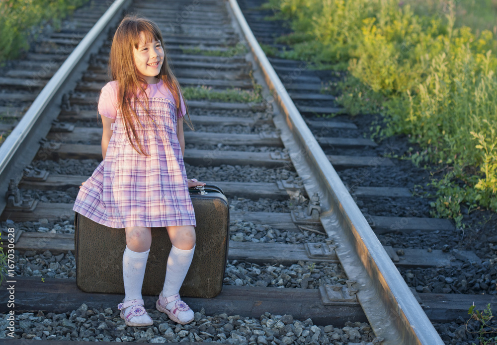 Little girl with a suitcase on the railway. The concept of travel. Retro style.