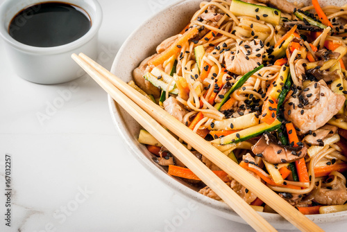 Traditional Asian food. Lunch stirfry: rice noodles, zucchini, carrots, bamboo, mushrooms, pork (beef), soy sauce and black sesame. With soy sauce, chopsticks. Copy space