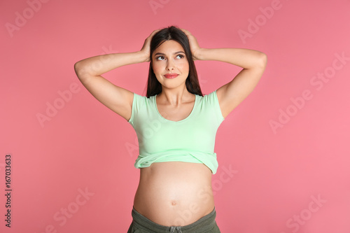 Young pregnant woman choosing name for baby on pink background