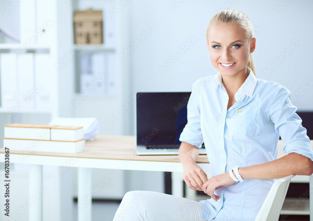 Attractive businesswoman sitting on a desk with laptop in the office Attractive businesswoman sitting on a desk with laptop in the office