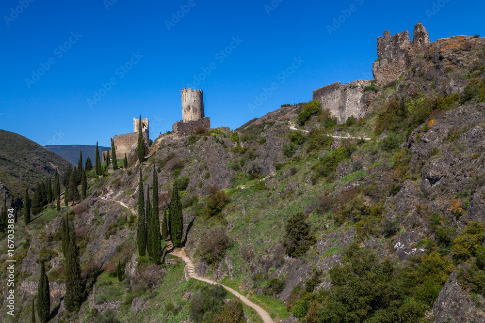 ruins of Lastrous castle in France on top of the mountain on a sunny day with trees and path