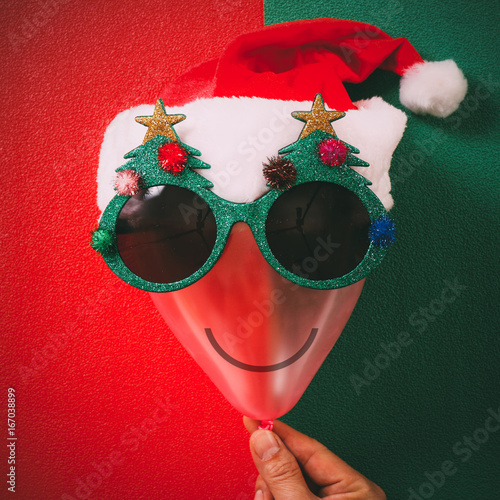 Hand holding Christmas glasses that decoration with Christmas tree and red hat on air bolloon   on green background photo