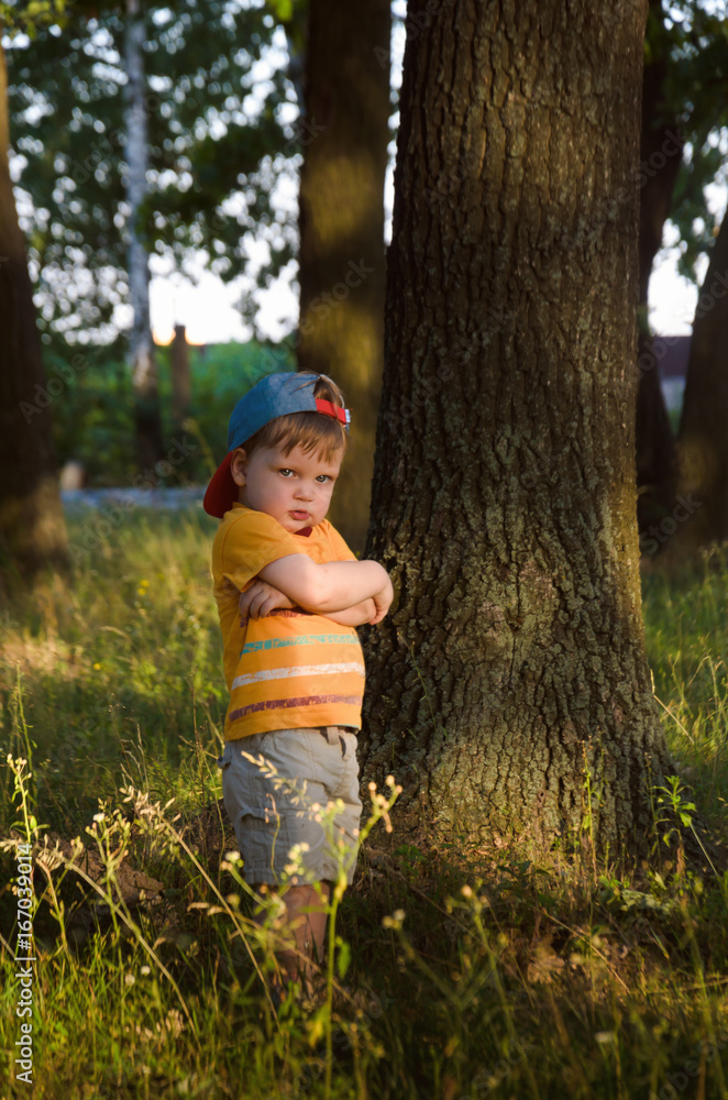 Sad offended boy stands under a tree with his arms crossed Sad offended boy stands under a tree with his arms crossed