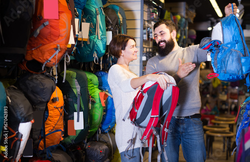 cheerful couple examining rucksacks in sports equipment store
