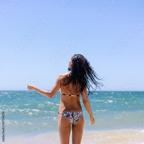 Attractive woman bathing playfully on a sunny summer holiday, joyful, coastal outdoors background. Travel lifestyle enjoying the sun on beach shore.