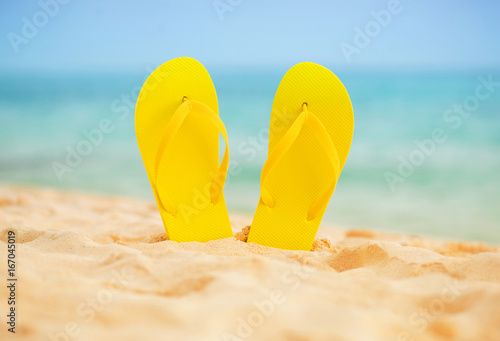 Yellow sandal flip flop on the white sand beach with blue sea and sky background in summer vacations copy space