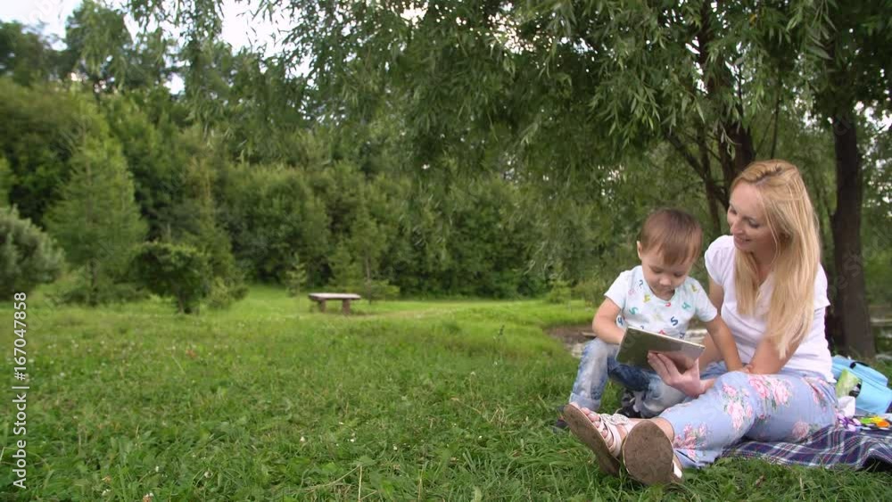 Young mother and little son spending day in the park. Woman and child using tablet computer. Young mother and little son spending day in the park. Woman and child using tablet computer.