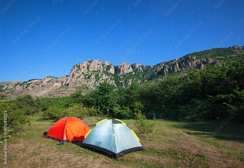Tourist tents in a clearing in the mountains against the starry sky and the mountain peak