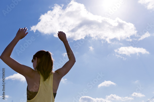 Attractive young woman stretching her arms while standing against a deep blue sky, exercising on a sunny day.
