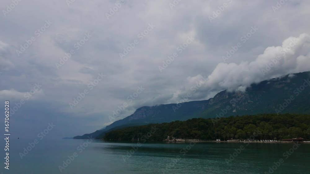 A dark, overcast shot of Akyaka shoreline (Gulf of Gokova, Mugla, Turkey) right after heavy rain. Low altitude cumulus clouds can be seen over the peaks of Sakar Mountain. A dark, overcast shot of Akyaka shoreline (Gulf of Gokova, Mugla, Turkey) right after heavy rain. Low altitude cumulus clouds can be seen over the peaks of Sakar Mountain.