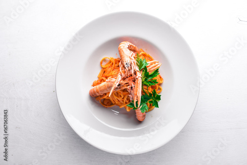 Pasta and tiger shrimp in tomato sauce. Italian traditional food. On a wooden background. Top view. Free space for your text. photo
