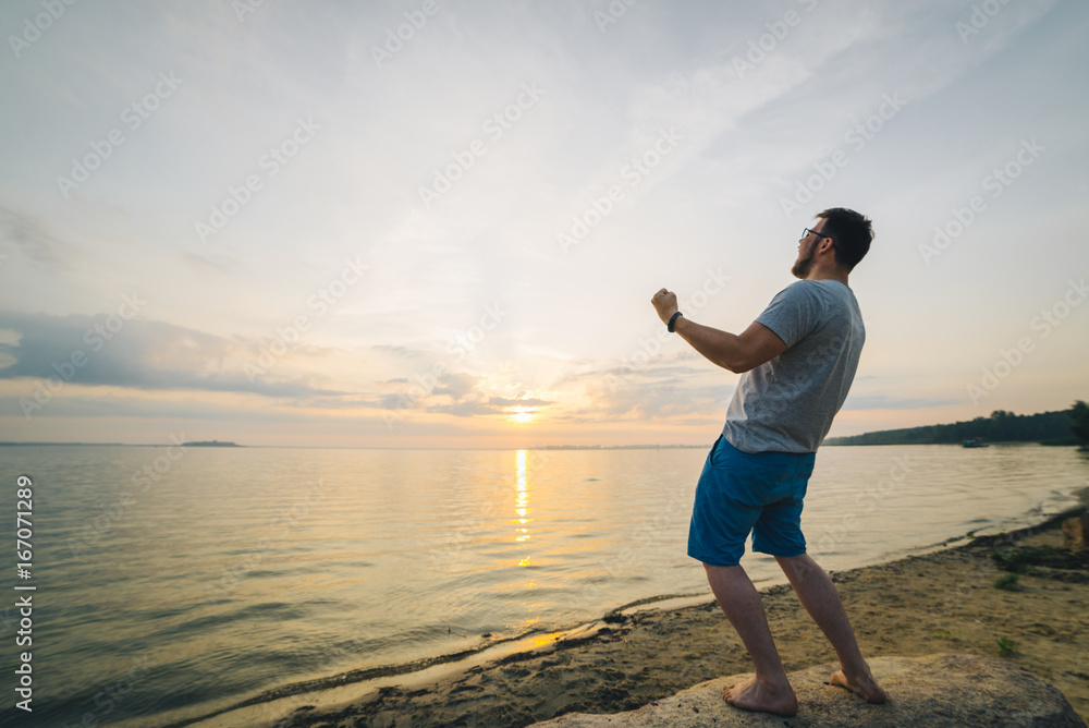 Fototapeta premium man on the beach looking on sunrise with hands up