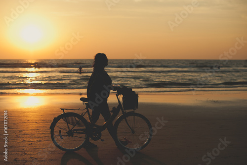 A woman makes an evening bike ride along the sea. People walk along the sea at sunset. Sunset on sea. Silhouette of people. Travelers at sunset. Tourists on vacation © MISHA