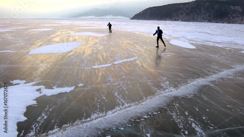 Two men are skating on the ice of frozen Lake Baikal during beautiful sunset.