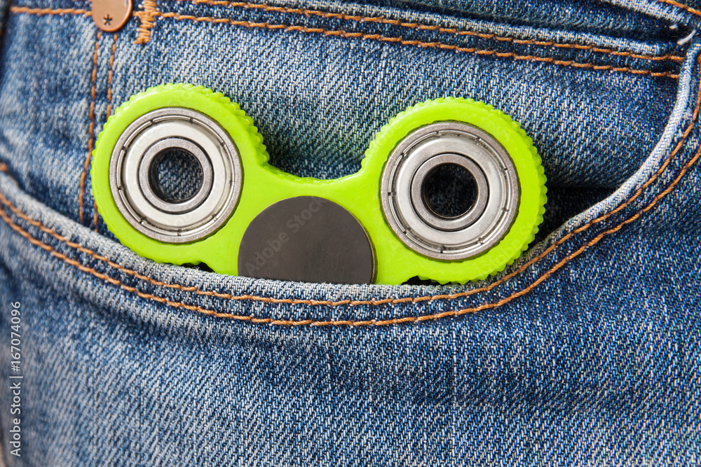 Green fidget spinner in the man's jeans pocket. Closeup. Selective focus. Green fidget spinner in the man's jeans pocket. Closeup. Selective focus.