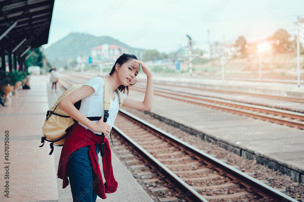 Young girl asian tourist standing with backpack waiting the train going to travel scenery town tour around at train station platform for take the rest, happy and life experience having fun