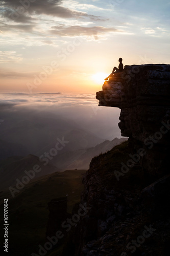 Woman sitting on the cliff and enjoying sunset