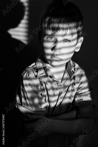 Black and white photo of a boy in a shirt in the shade of the blinds