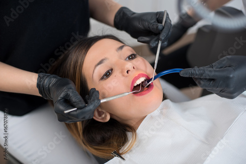 Beautiful girl having dental check up in dental clinic. Dentist examining a patient s teeth with dental tools - mirror and probe. Dentistry.