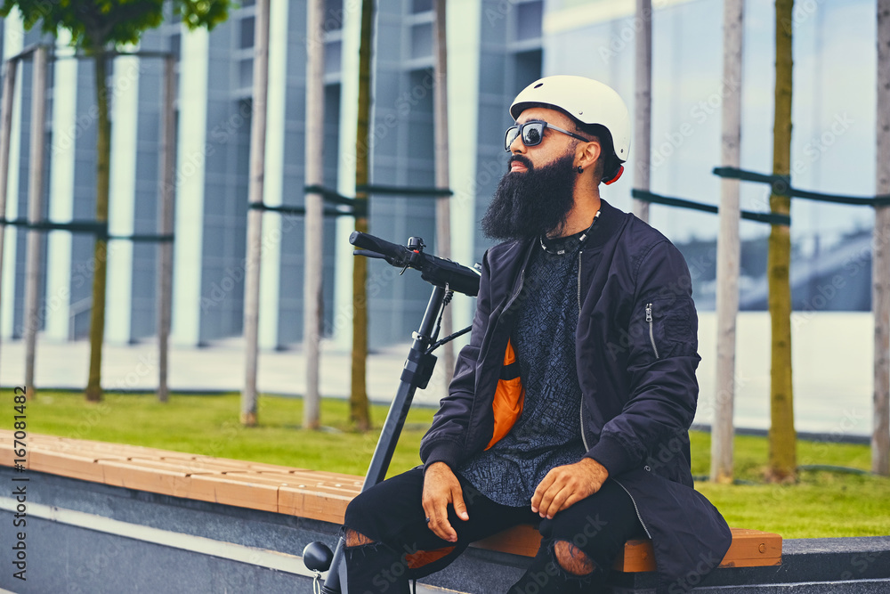 A man relaxing on a bench after riding by electric scooter. A man relaxing on a bench after riding by electric scooter.
