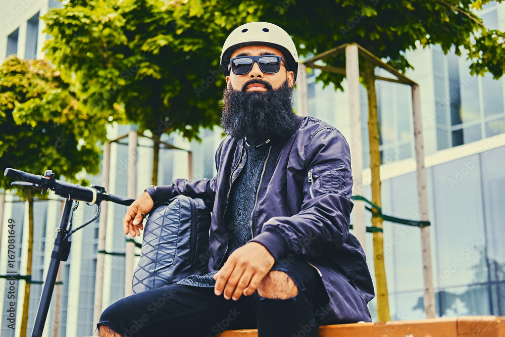 A man relaxing on a bench after riding by electric scooter. A man relaxing on a bench after riding by electric scooter.