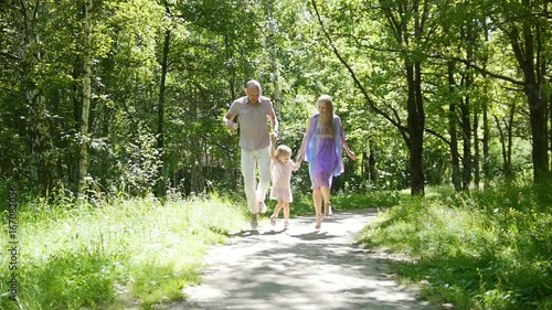 Happy family have fun in park - father, mother and little daughter is jumping on one leg, slow-motion photo