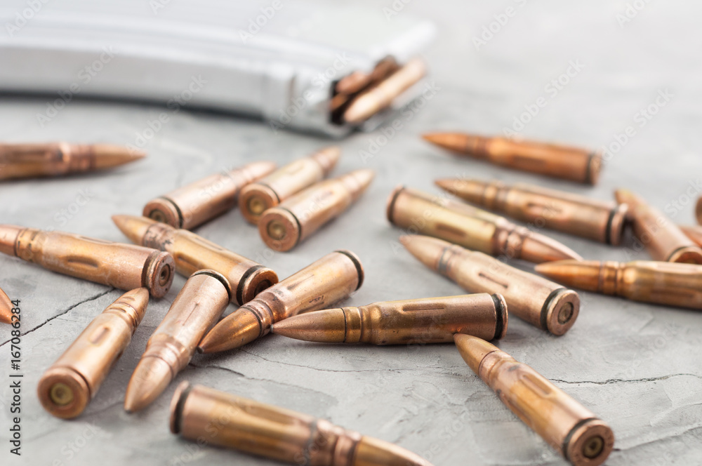Silver full magazine for assault rifle and scattered bullets on old grey broken concrete Silver full magazine for assault rifle and scattered bullets on old grey broken concrete