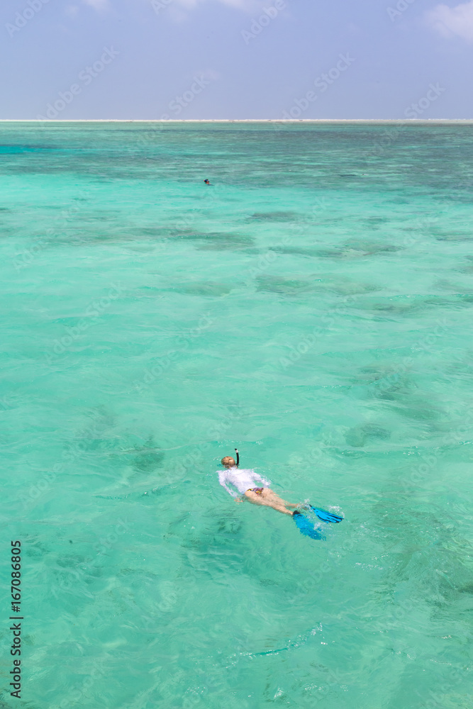 Woman snorkeling in clear shallow sea of tropical lagoon with turquoise blue water and coral reef, near exotic island. Mnemba island, Zanzibar, Tanzania.
