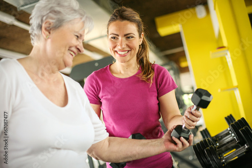 Personal trainer working exercise with senior woman in the gym. Woman picking weight. Workout in gym