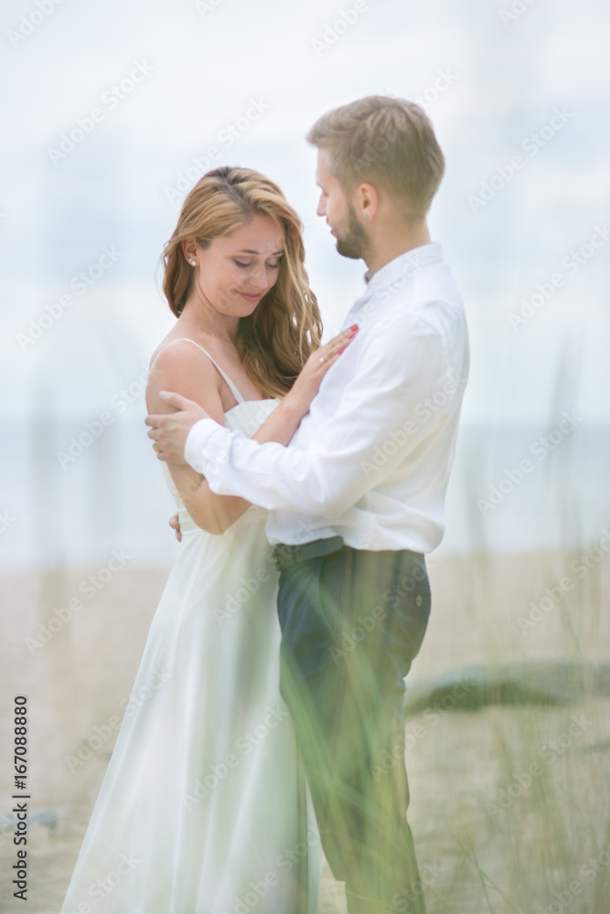 Young happy just married couple walking holding hands on the beach along the sea on summer evening Young happy just married couple walking holding hands on the beach along the sea on summer evening