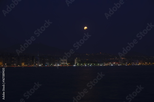 August full moon over Thessaloniki,Greece waterfront. Moon rising over White Tower landmark seen from the city port.