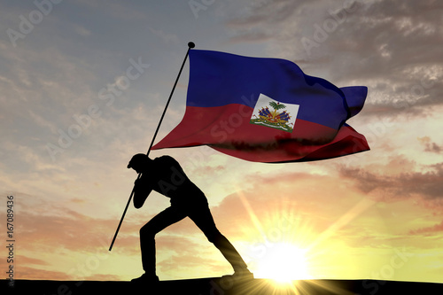 Fényképezés Haiti flag being pushed into the ground by a male silhouette