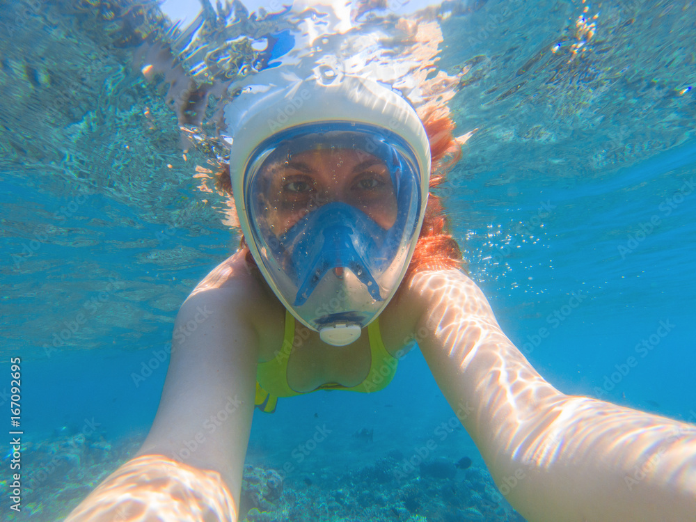 Fototapeta premium Snorkeling in full face mask. Summer activity. Beautiful girl in shallow seawater.