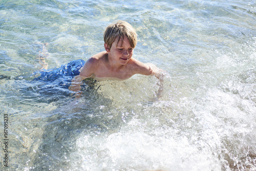 Young child boy having fun in the sea on the waves and enjoying water in summer holiday