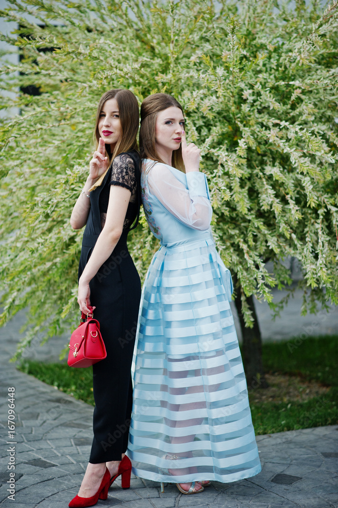 Two fabulous young women in gorgeous fashionable dresses posing in the park on the graduation day. Two fabulous young women in gorgeous fashionable dresses posing in the park on the graduation day.