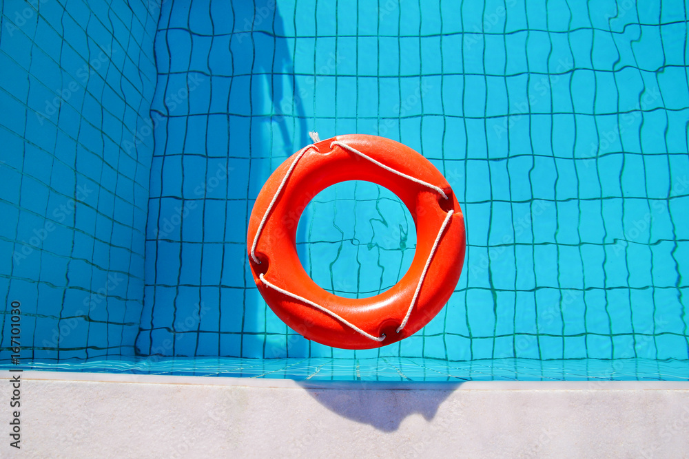 Red lifebuoy pool ring float, ring floating in refreshing blue swimming pool. Red float floating in the pool with blue water. Inflatable red swim ring floating on a pure water with sunny reflections.