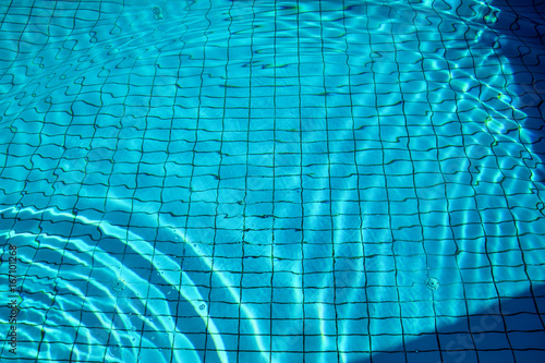 Swimming pool bottom caustics ripple and flow with waves background. Surface of blue swimming pool, background of water in swimming pool. Clear light blue pool water ripples with sun reflections.