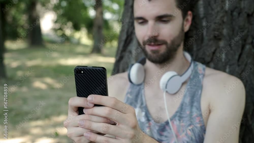 Handsome man leaning on the tree in the park and texting on smartphone, steadycam shot
Handsome man leaning on the tree in the park and texting on smartphone, steadycam shot