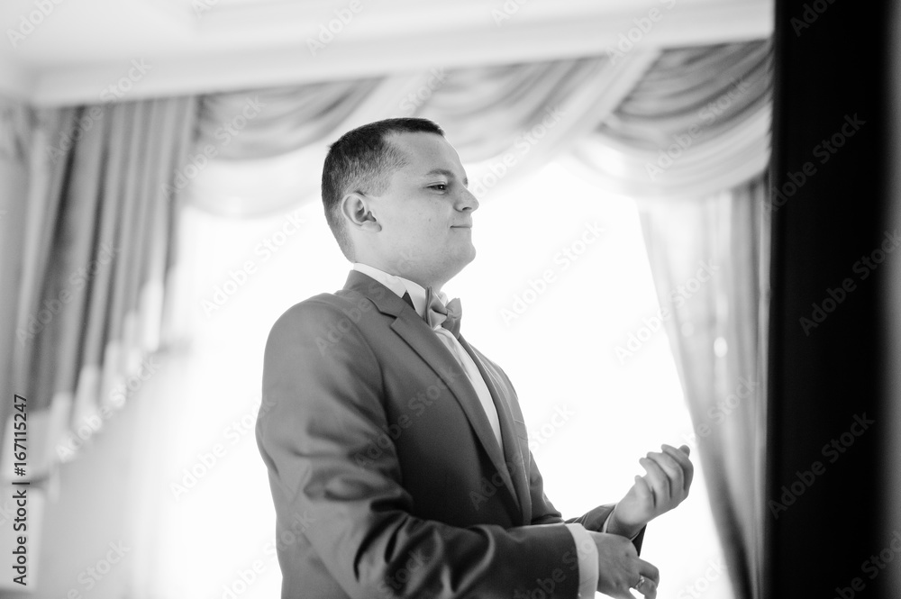 Handsome groom in red tuxedo posing in his room on a wedding day. Black and white photo. Handsome groom in red tuxedo posing in his room on a wedding day. Black and white photo.