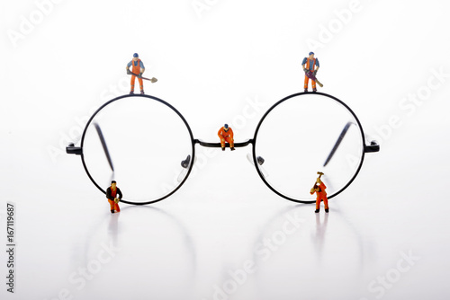 Miniature people workers walk by glasses over white background.