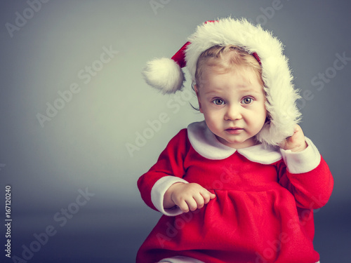 portrait of little caucasian baby girl dressed as santa claus, gray background studio shot.