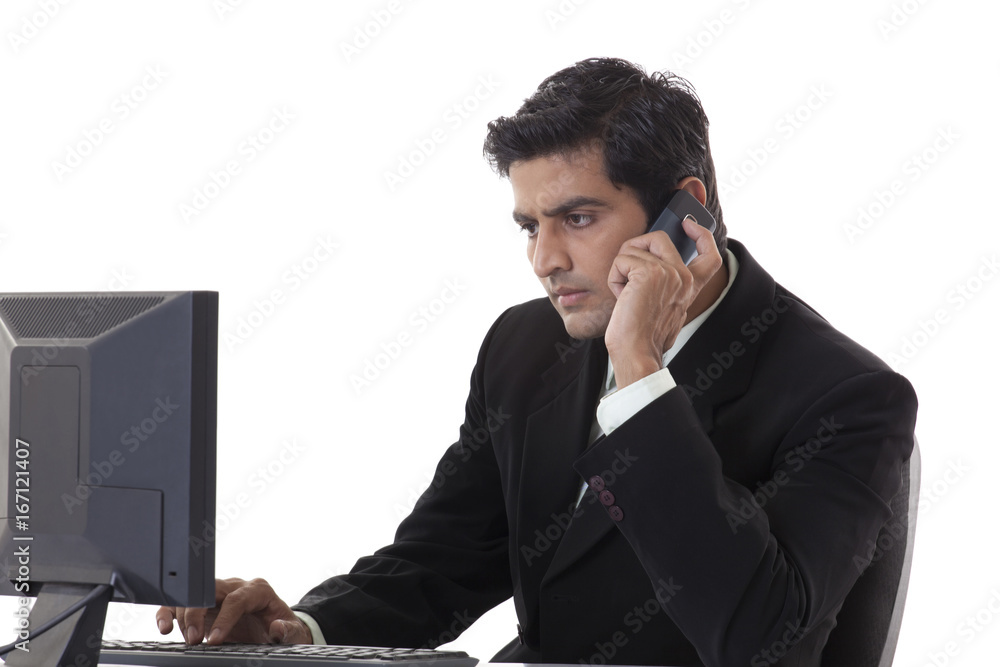 Young businessman working on computer while using cell phone Young businessman working on computer while using cell phone