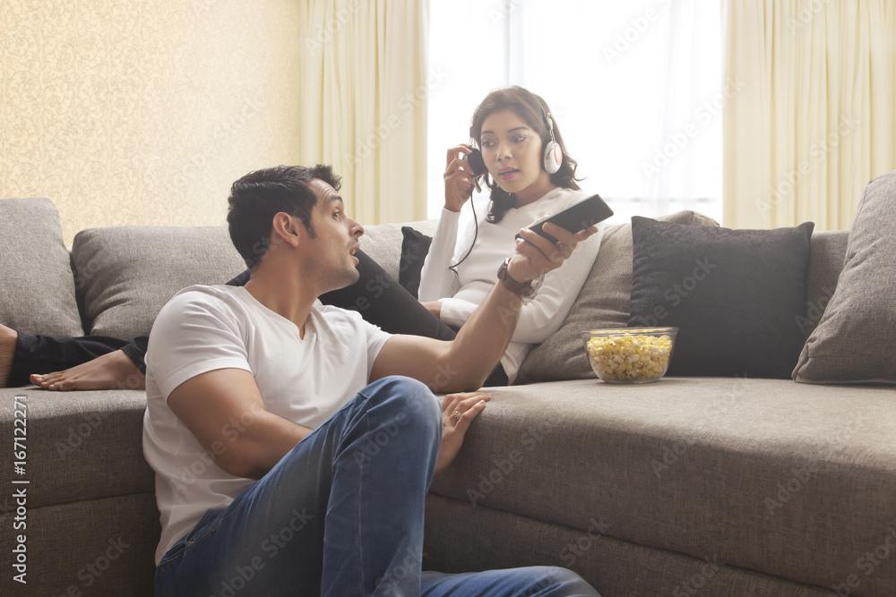 Young man watching TV while woman listening music sitting on sofa