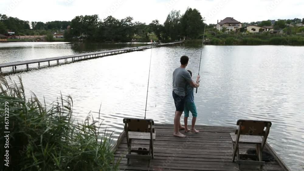 Father and son angling at tranquil lake in summer Father and son angling at tranquil lake in summer